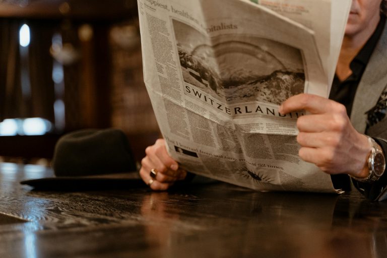 Close-up of man reading newspaper with focus on Switzerland headline.
