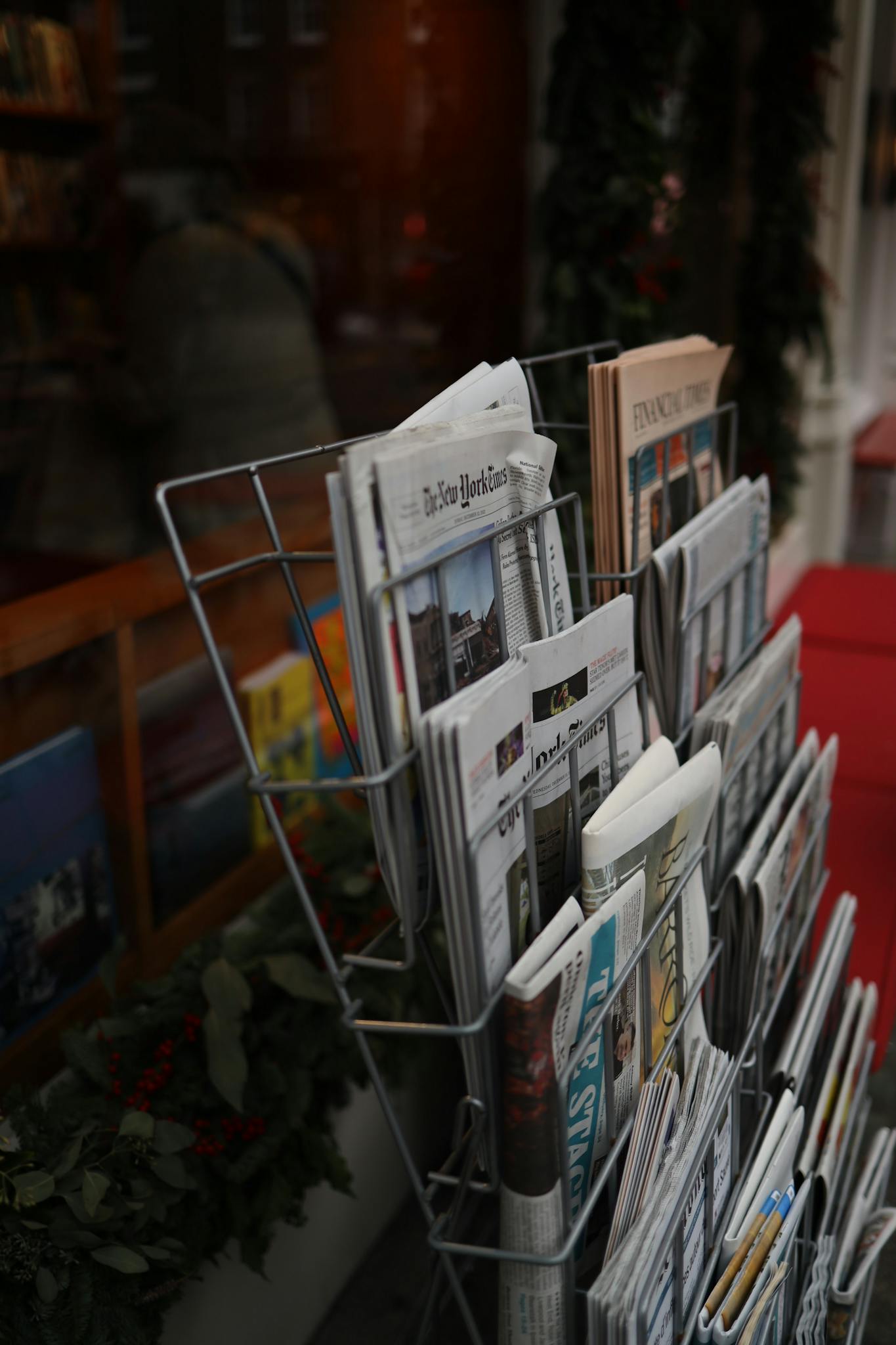 Street newsstand display featuring a range of newspapers and magazines in a cozy, urban setting.